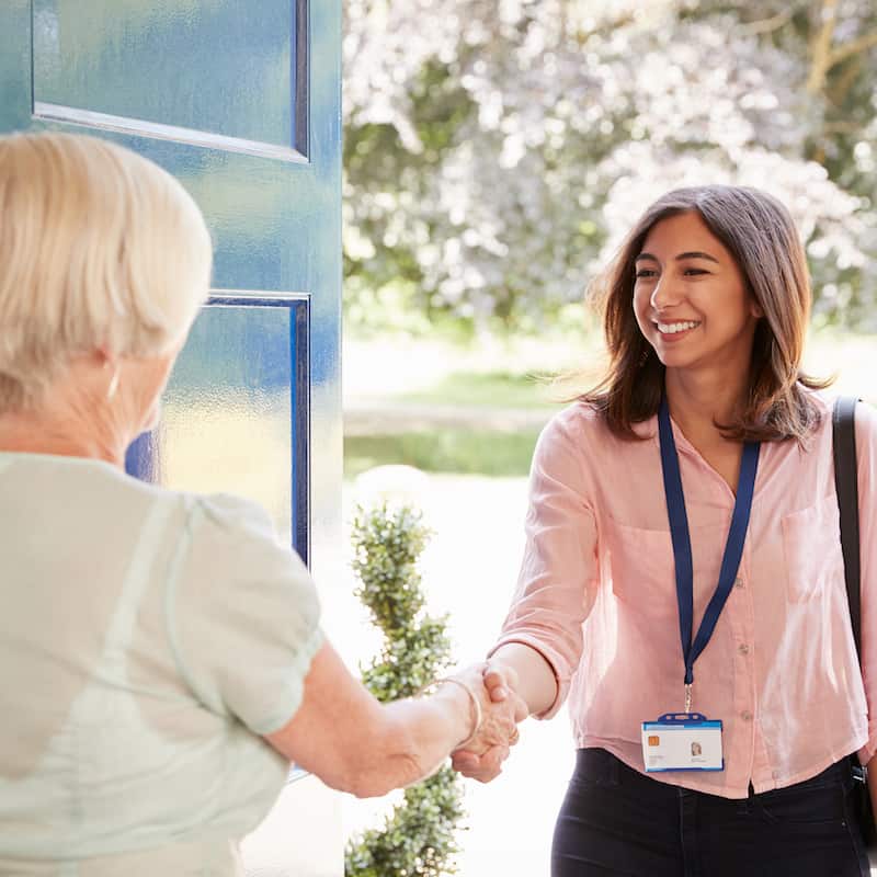 Senior woman greeting female care worker making home visit